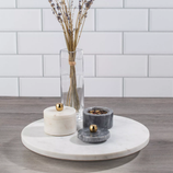 Marble spice containers with gold knobs sit on a round marble platter, accompanied by a clear vase holding dried lavender.