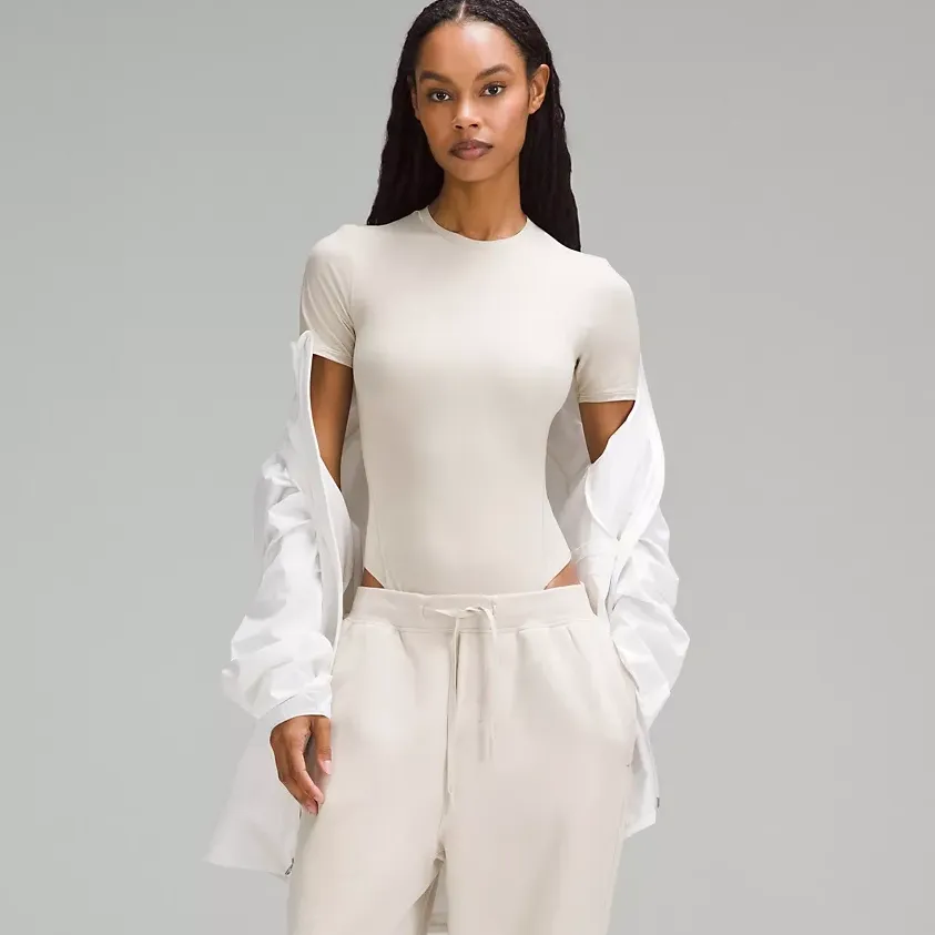 A fitted, cream-colored bodysuit with cut-out details on the shoulders and long, translucent sleeves with gathered cuffs.