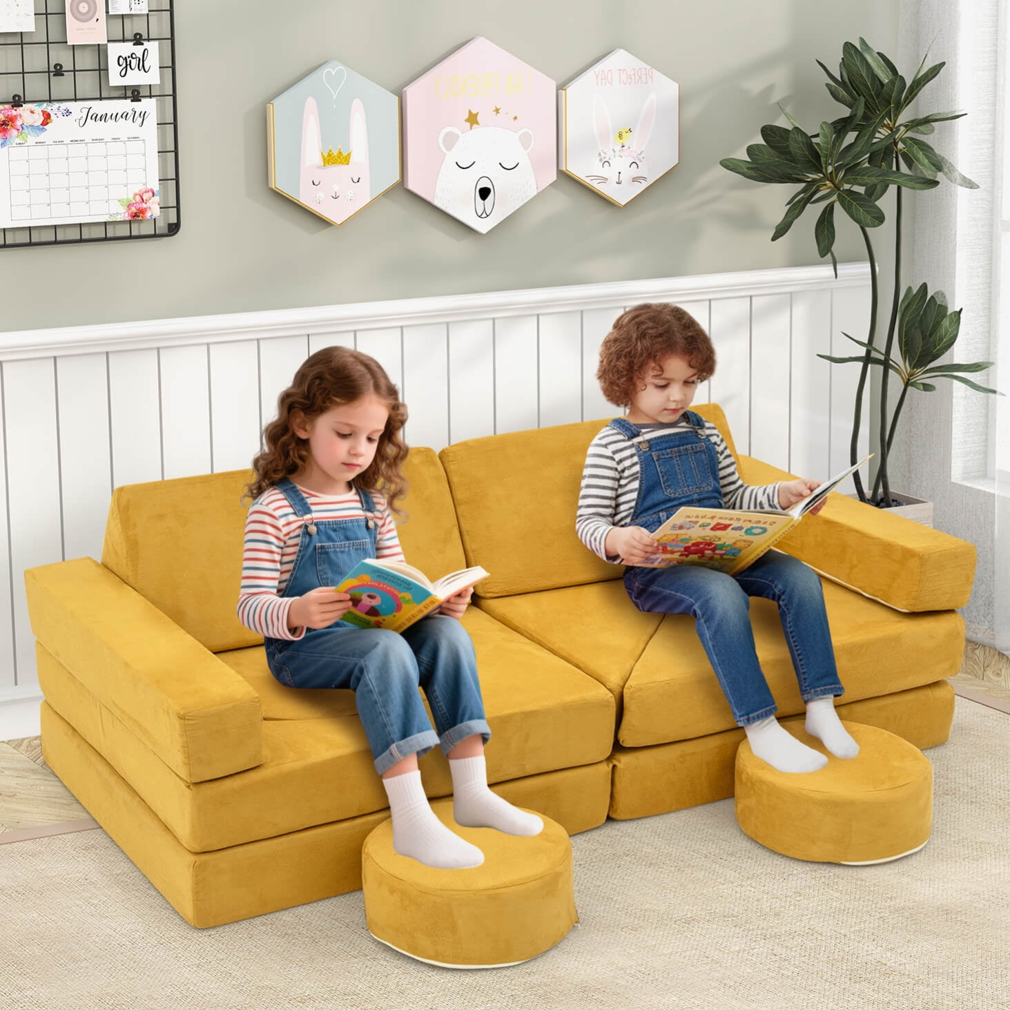 Two children sit on a modular yellow sofa with matching footstools, reading books. The setting includes decorative wall art and a potted plant by the window.