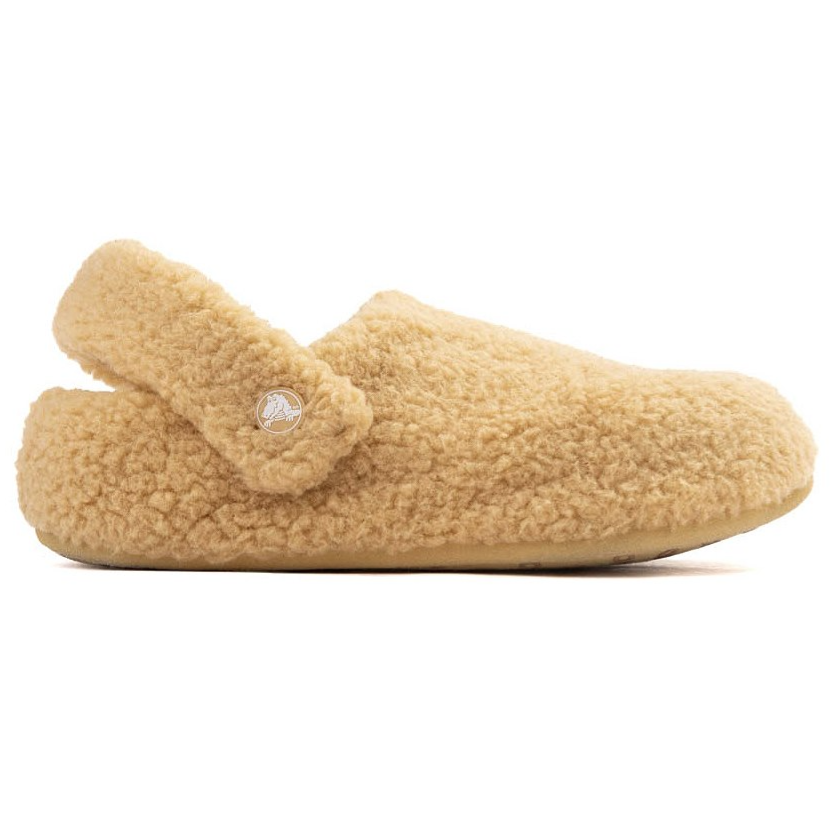 A beige, fluffy slipper with a strap is pictured, adorned with a small circular emblem on the side.
