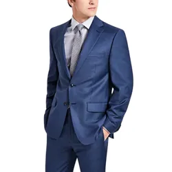 A man is wearing a blue suit with a gray dress shirt and a patterned tie, standing with hands in pockets.