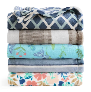 A stack of five folded blankets with various patterns: blue and white diamond, plaid, blue with butterflies, striped blue, and floral.