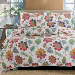 A colorful floral queen quilt set featuring vibrant, multicolored flowers and leaves on a white background, accompanied by matching shams and decorative pillows.