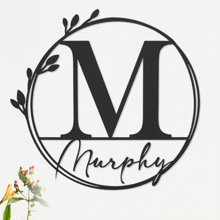 A decorative wall art piece featuring the letter \“M\“ in a circle with botanical accents, accompanied by the name \“Murphy,\“ displayed above a sofa with flowers nearby.