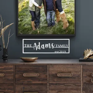 A personalized name plaque featuring \“The Adams Family\“ with \“est. 2019\“ below, in a clean, bold font encased in a dark frame.