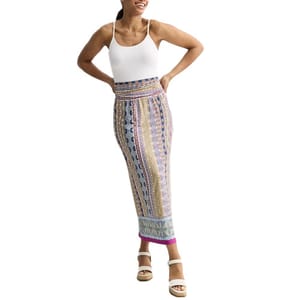 A woman wears a fitted, colorful patterned skirt with a high waist, paired with a white tank top and white sandals.