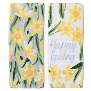 Two kitchen towels feature a yellow daffodil print. One towel shows an all-over floral pattern, while the other has the words \“Happy Spring\“ alongside the flowers.