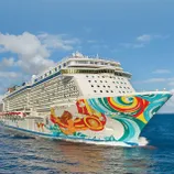 A cruise ship with vibrant, colorful artwork on its hull, sailing on open blue water under a partly cloudy sky.