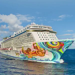 A cruise ship with vibrant, colorful artwork on its hull, sailing on open blue water under a partly cloudy sky.