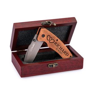 A folding knife with a wooden handle engraved with intertwined hearts, the name \“Richard,\“ and the date \“02.14.2023\“ is displayed in an open wooden box with a clasp.
