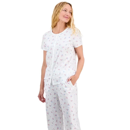 A woman is wearing a short-sleeve pajama set with a floral pattern, featuring a button-front top and matching pants, both in light, airy fabric.