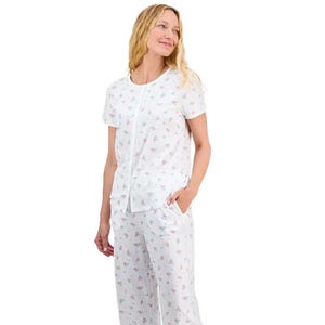 A woman is wearing a short-sleeve pajama set with a floral pattern, featuring a button-front top and matching pants, both in light, airy fabric.