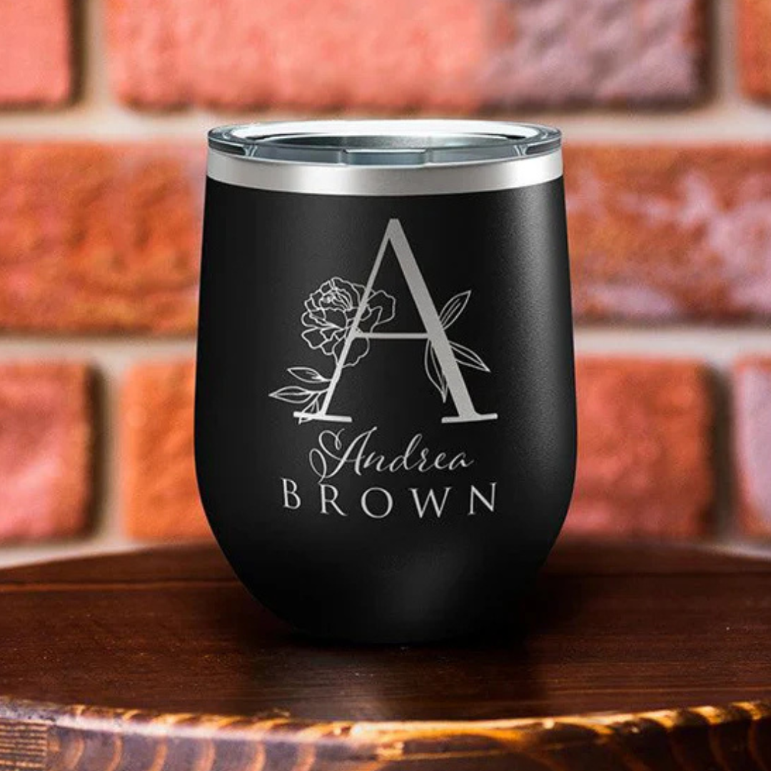 A black stainless steel tumbler with a silver lid, featuring a large letter \“A\“ accompanied by a floral design, and the name \“Andrea Brown\“ engraved below.