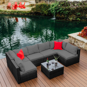 Outdoor sectional wicker sofa with cushions and a matching coffee table, set near a body of water.