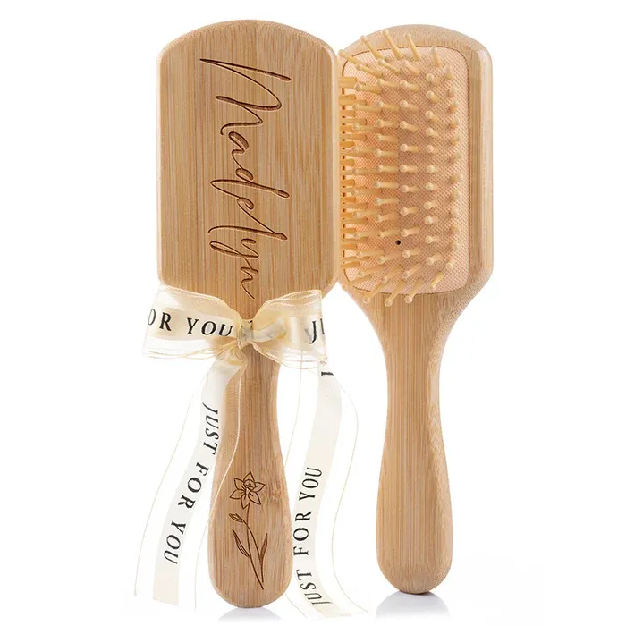 Two bamboo paddle hairbrushes are shown, one engraved with the name \“Madelyn\“ and decorated with a ribbon that reads \“Just For You.\“
