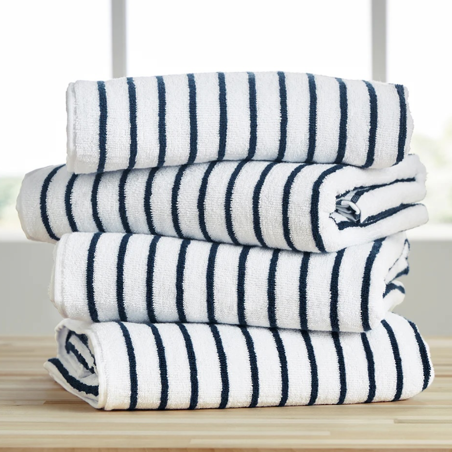 A stack of four folded white towels with navy blue stripes, placed on a wooden surface in front of a window.