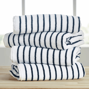 A stack of four folded white towels with navy blue stripes, placed on a wooden surface in front of a window.
