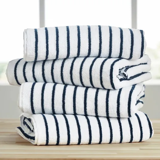 A stack of four folded white towels with navy blue stripes, placed on a wooden surface in front of a window.