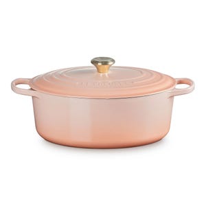 Pink enameled cast iron Dutch oven with a matching lid and gold knob, featuring side handles.