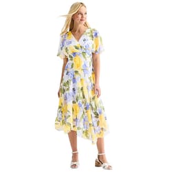 A woman wears a floral wrap dress featuring yellow and blue hues, knee-length with short sleeves, paired with white sandals.