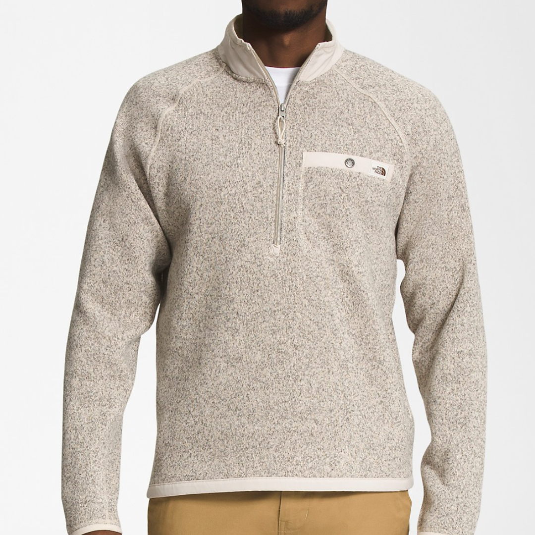 A person is wearing a beige fleece pullover with a half-zip closure and a logo patch on the chest.