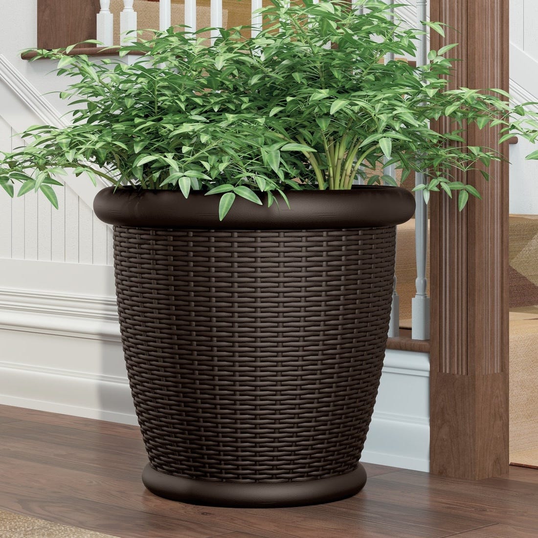 A large, dark brown, woven-style planter with lush green foliage sits on a wooden floor near a staircase railing.