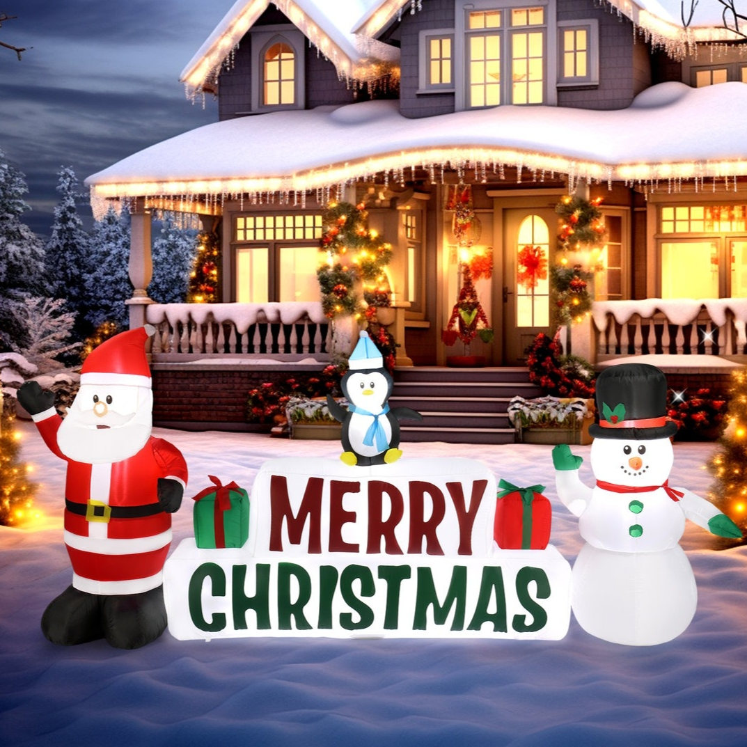 Festive Christmas yard decorations featuring inflatable Santa, penguin, and snowman alongside a \“Merry Christmas\“ sign in front of a snow-covered, decorated house.