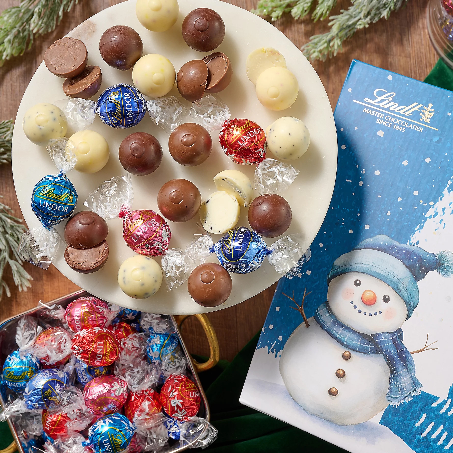 125ct Lindt Lindor Holiday Truffles feature a festive mix of milk, white, and assorted chocolate truffles in colorful wrappers, accompanied by a snowman-themed holiday box.