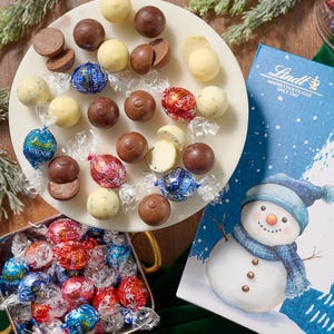 125ct Lindt Lindor Holiday Truffles feature a festive mix of milk, white, and assorted chocolate truffles in colorful wrappers, accompanied by a snowman-themed holiday box.