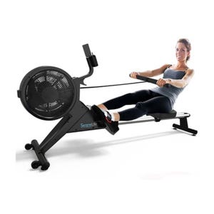 A person is exercising on a SereneLife magnetic rowing machine, featuring an adjustable resistance system, ergonomic seat, and LCD display.