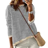 A person is wearing a striped black and white sweater with a light brown trim, paired with light pants and carrying a woven crossbody bag.