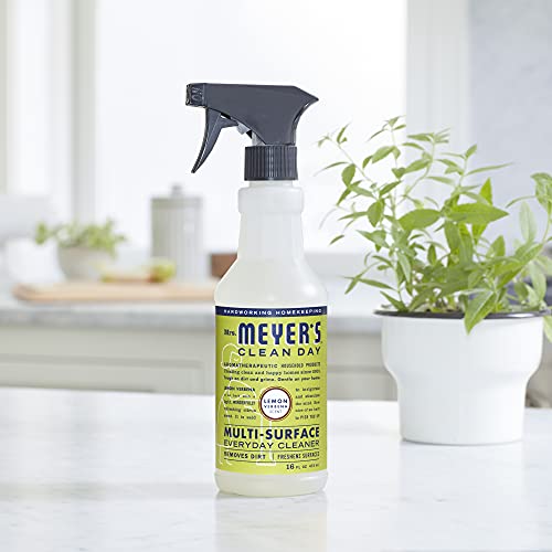 A bottle of Mrs. Meyer's Clean Day multi-surface everyday cleaner with a spray nozzle, set on a counter near a potted plant.