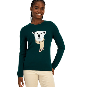 A person is wearing a green sweater featuring a graphic of a bear with a scarf on the front, paired with light-colored pants.