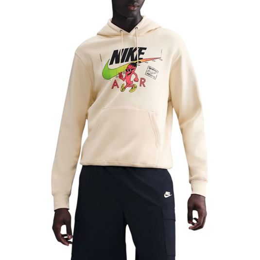 Model in a Nike outfit featuring a cream hoodie with graphic print, black shorts with a Nike logo, black socks, white sneakers, and a black cap.