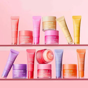 Assorted Laneige skincare products, including jars and tubes in vibrant pink, orange, purple, and yellow hues, are neatly arranged on shelves against a pink background.