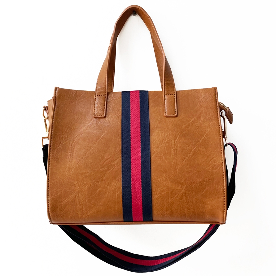 Brown faux-leather tote with dual handles, featuring a vertical navy and red stripe on the front. It includes a detachable shoulder strap with matching colors.