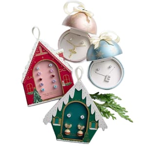 Brilliance Holiday Jewelry Sets feature festive packaging with red and green house shapes and two dome boxes. They include cubic zirconia stud earrings and charm necklaces, all with silver or gold plating.
