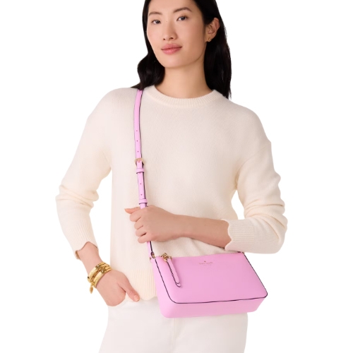 A woman wearing a cream sweater carries a pink crossbody bag. She also wears multiple gold bracelets on her left wrist.
