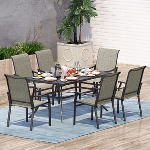 The 7pc Patio Dining Set features a rectangular black table with six green cushioned chairs, ideal for outdoor dining. It rests on a light blue rug, surrounded by plants, and is set with dishes, glasses, and decorative items.