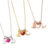 Three necklaces feature gold, silver, and rose gold chains, each with two letters and a colored heart charm: pink with \“S\“ and \“B,\“ red with \“L\“ and \“C,\“ and white with \“E\“ and \“L.\“