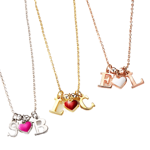 Three necklaces feature gold, silver, and rose gold chains, each with two letters and a colored heart charm: pink with \“S\“ and \“B,\“ red with \“L\“ and \“C,\“ and white with \“E\“ and \“L.\“