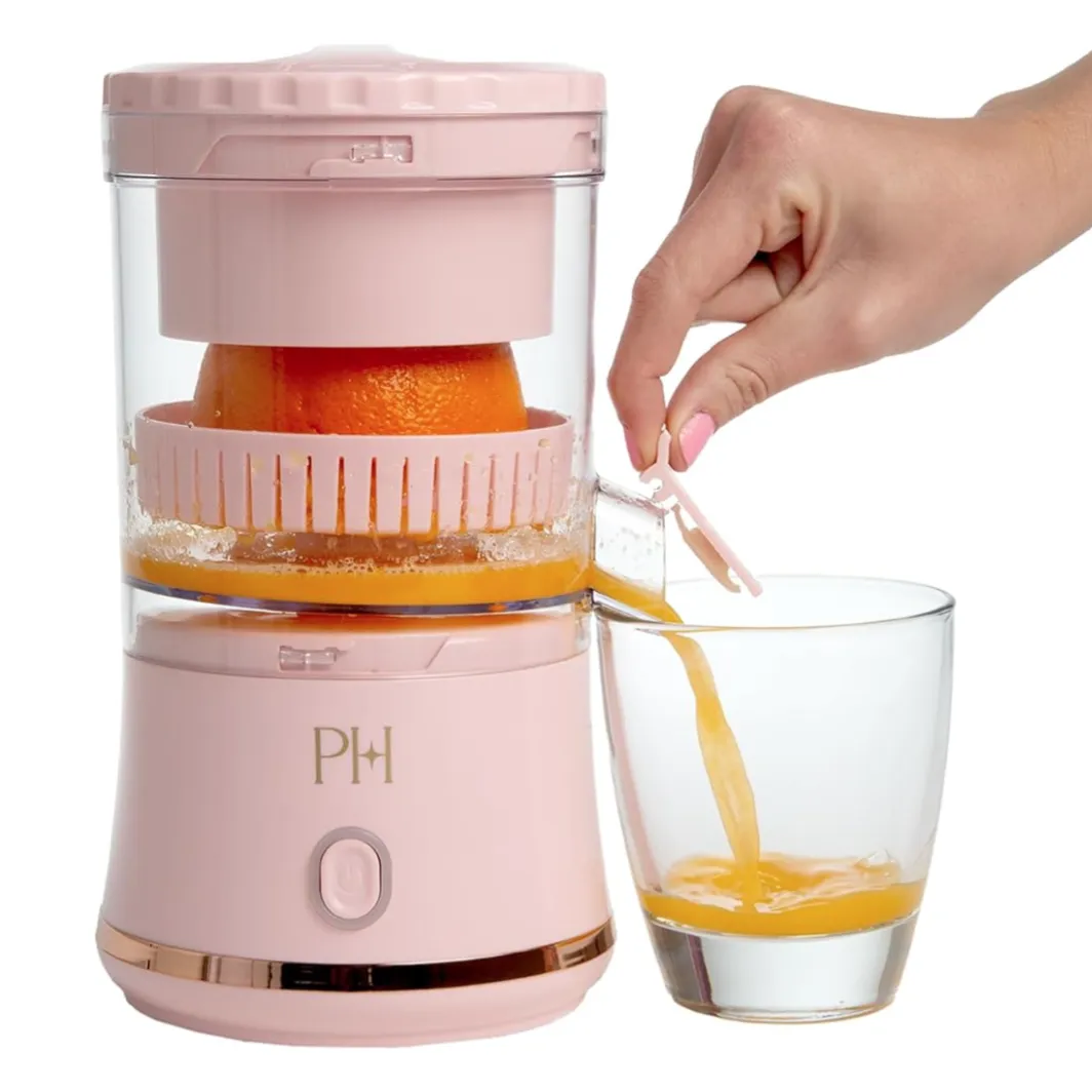 A pink electric citrus juicer is being used to extract juice from an orange, with the juice pouring into a glass.