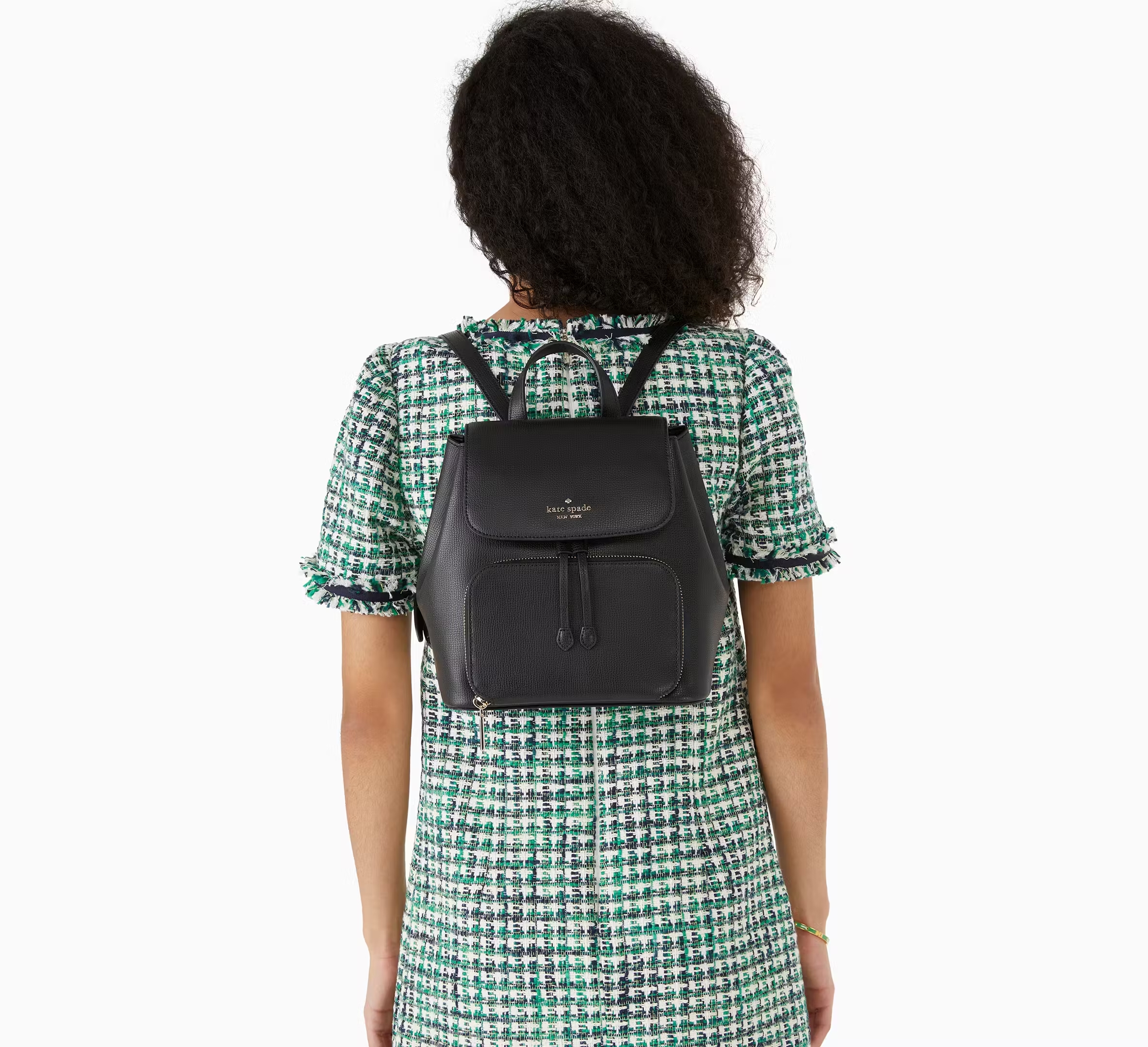 A woman wearing a houndstooth dress carries a black leather Kate Spade backpack.