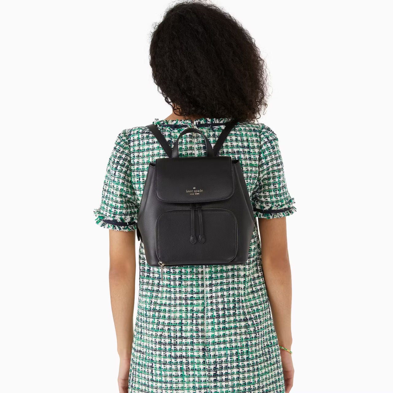 A woman wearing a houndstooth dress carries a black leather Kate Spade backpack.
