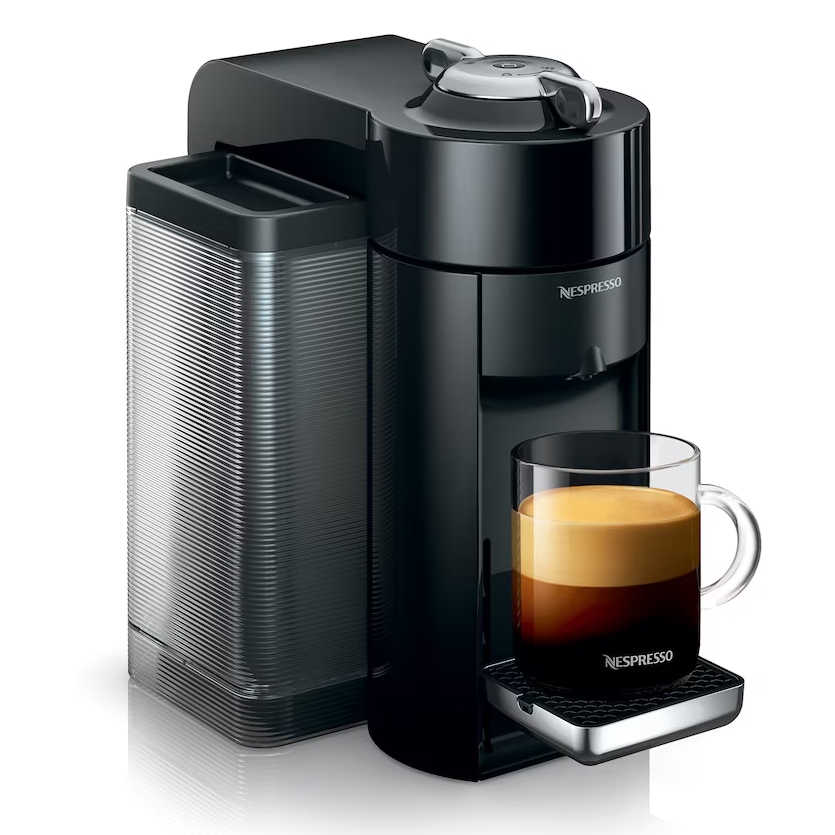 Nespresso espresso machine in black with an attached water tank and cup holder, featuring a glass mug filled with freshly brewed coffee and crema.
