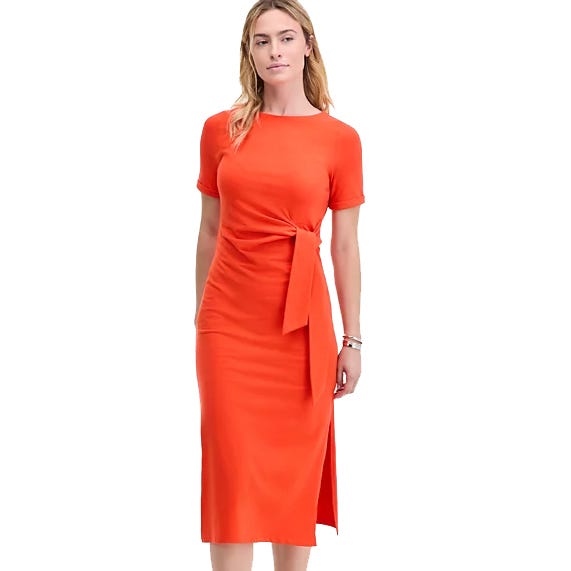 Woman wearing a knee-length, short-sleeved, orange dress with a side tie and side slit.