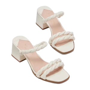White block-heeled sandals with two braided straps, featuring a square open toe and a slightly cushioned pink insole.