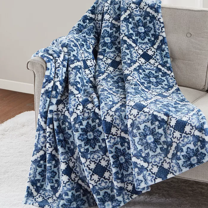 A blue and white floral patterned quilt is draped over a beige armchair.