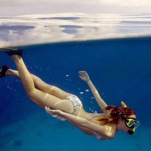 A woman is snorkeling underwater wearing a colorful bikini and flippers, with a snorkel mask and breathing tube.