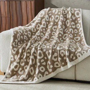 A beige and white leopard print blanket draped over a light-colored sofa, with a wooden cabinet and decorative items in the background.